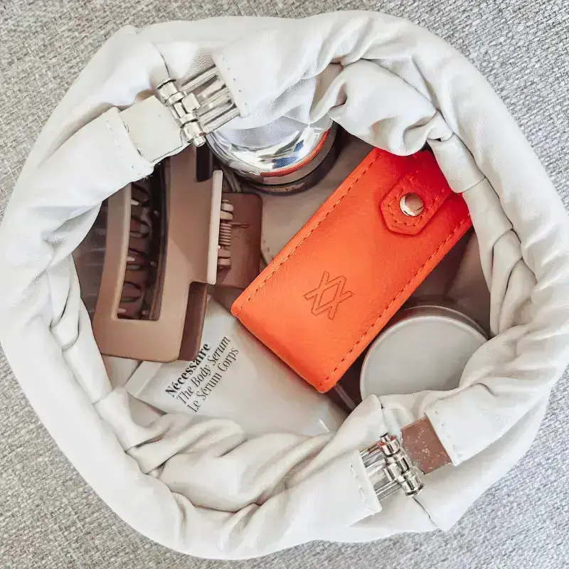 Open makeup bag with cosmetic items including an orange jewellery box