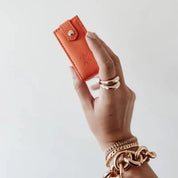 Hand holding an orange travel jewellery box against a plain background