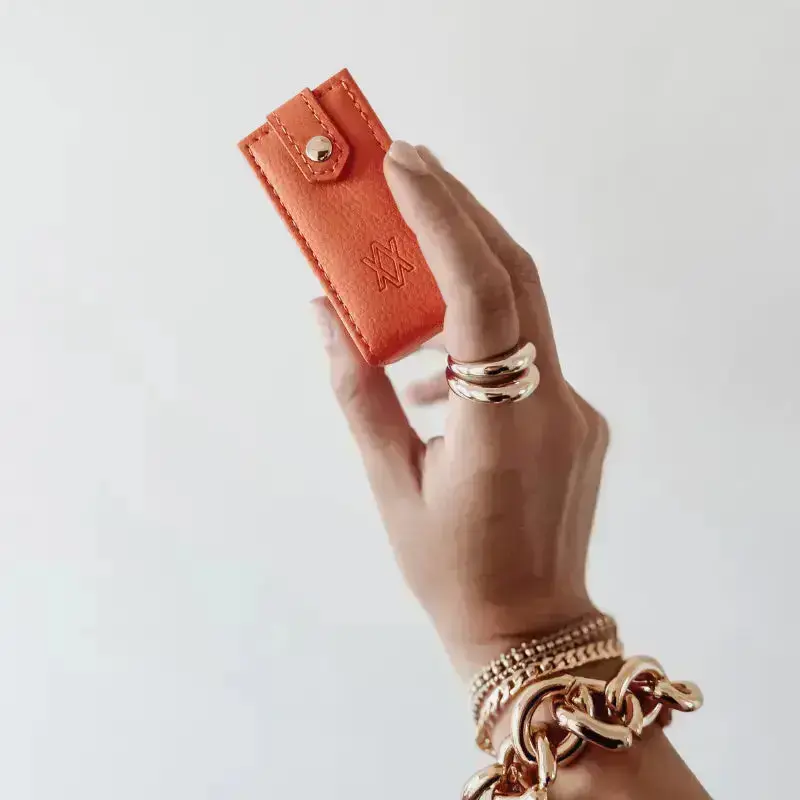 Hand holding an orange travel jewellery box against a plain background