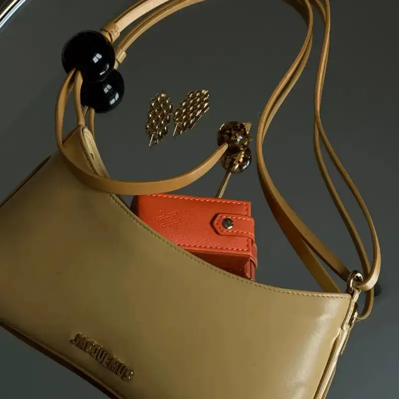 Beige handbag, black earrings, and an orange jewellery case on a dark background