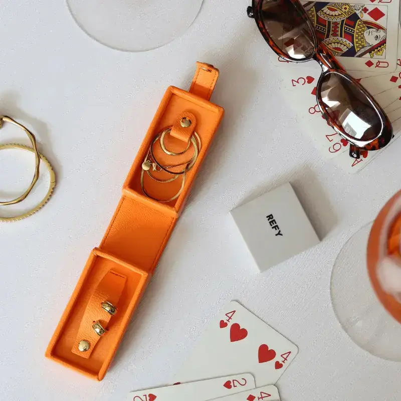 Orange jewelry box with gold rings, playing cards, and sunglasses on a white surface.