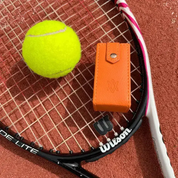 Tennis racket with a ball and orange jewellery case on a clay court