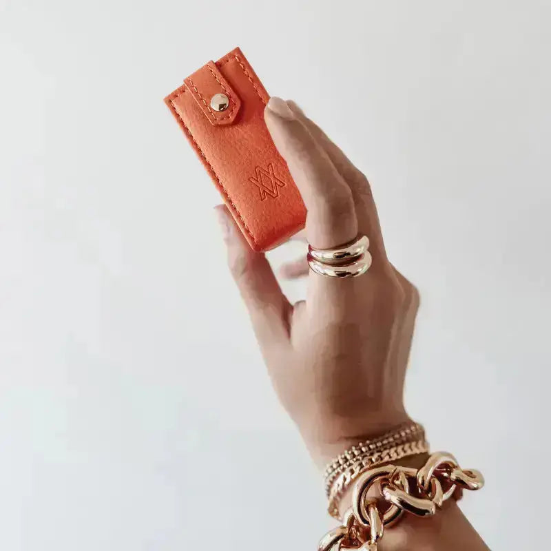Hand holding an orange travel jewellery box against a plain background